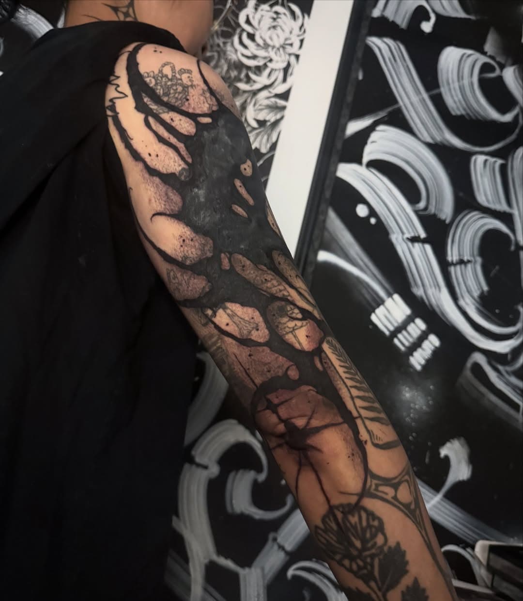 Heavy freehand blackwork blasted over an existing full sleeve, with solid black masses breaking around the older tattoos underneath.