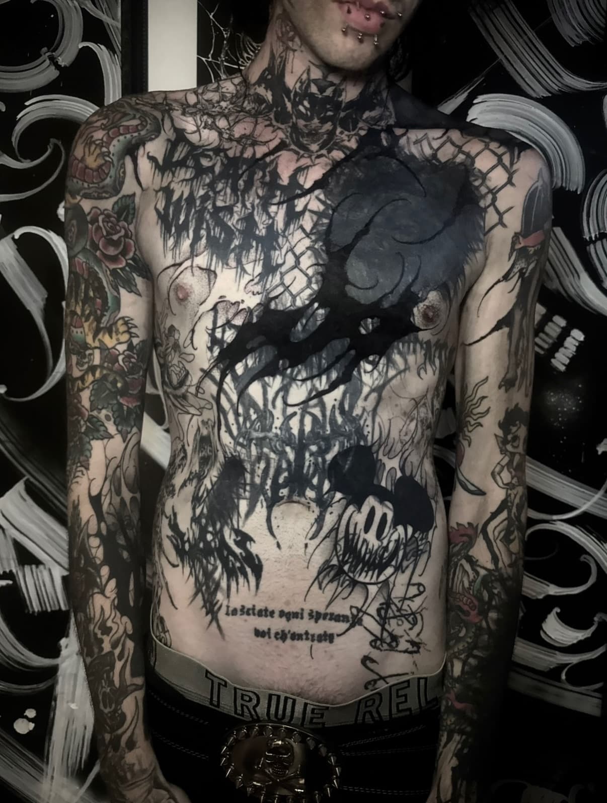 Gothic blackwork and lettering covering the chest and stomach, with a large solid black mass anchoring the centre.