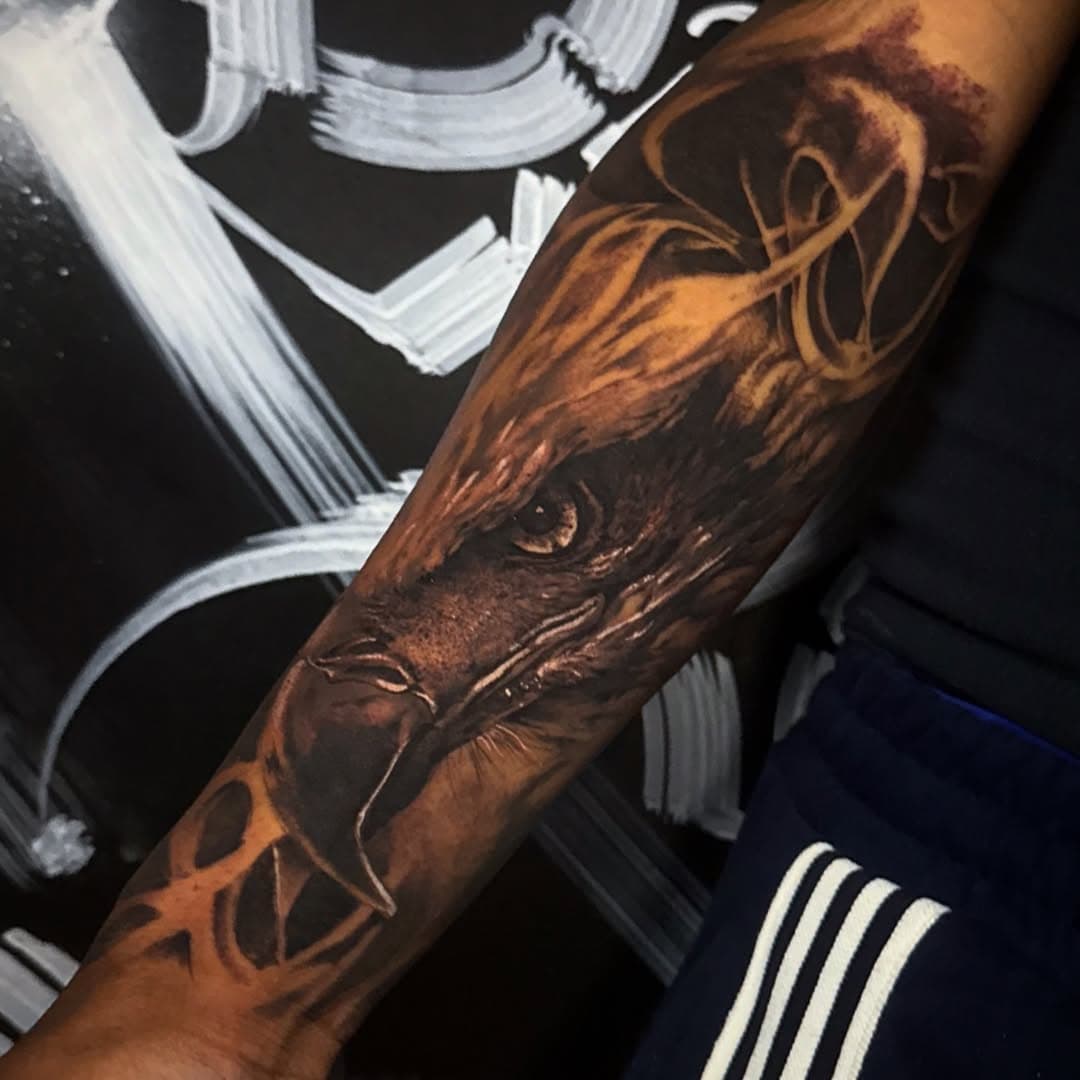 Black-and-grey realism eagle head filling the forearm, framed by smooth abstract ribbons of shading.