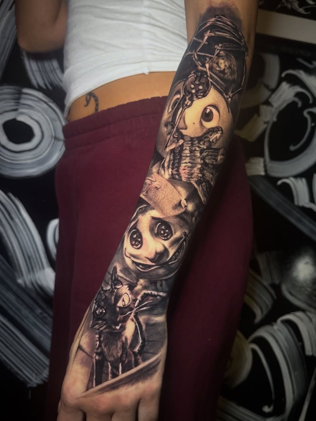 Black-and-grey sleeve running from elbow to hand with three stitched, button-eyed characters stacked down the forearm.
