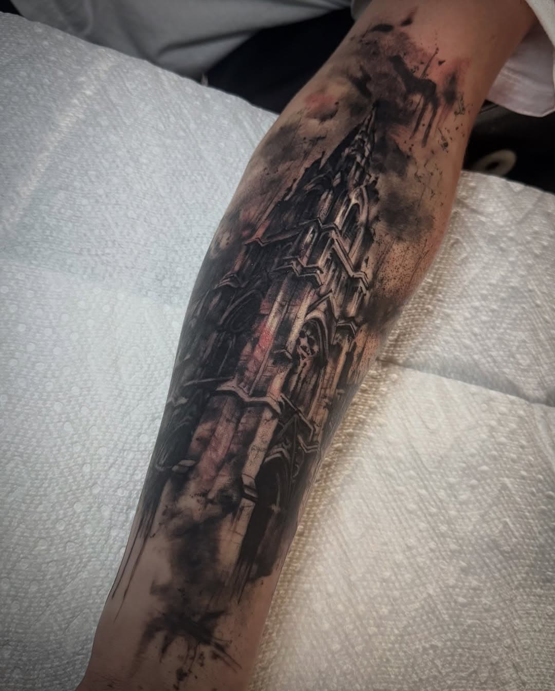 Black-and-grey gothic cathedral spire tattooed down the calf with smoke and ink-wash texture around the architecture.