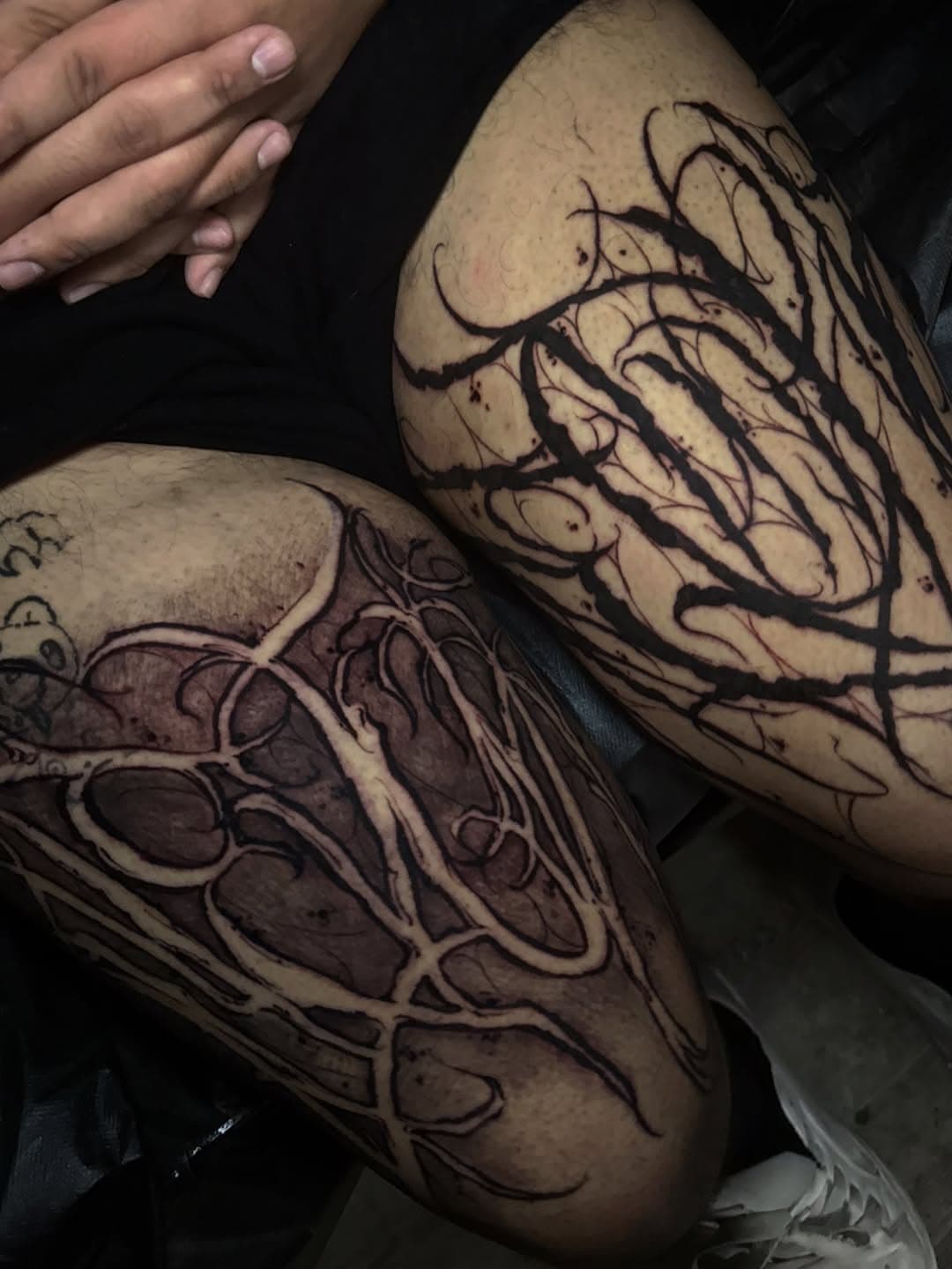 Gothic script lettering tattooed across both upper legs in long tapered strokes that follow the shape of each thigh.