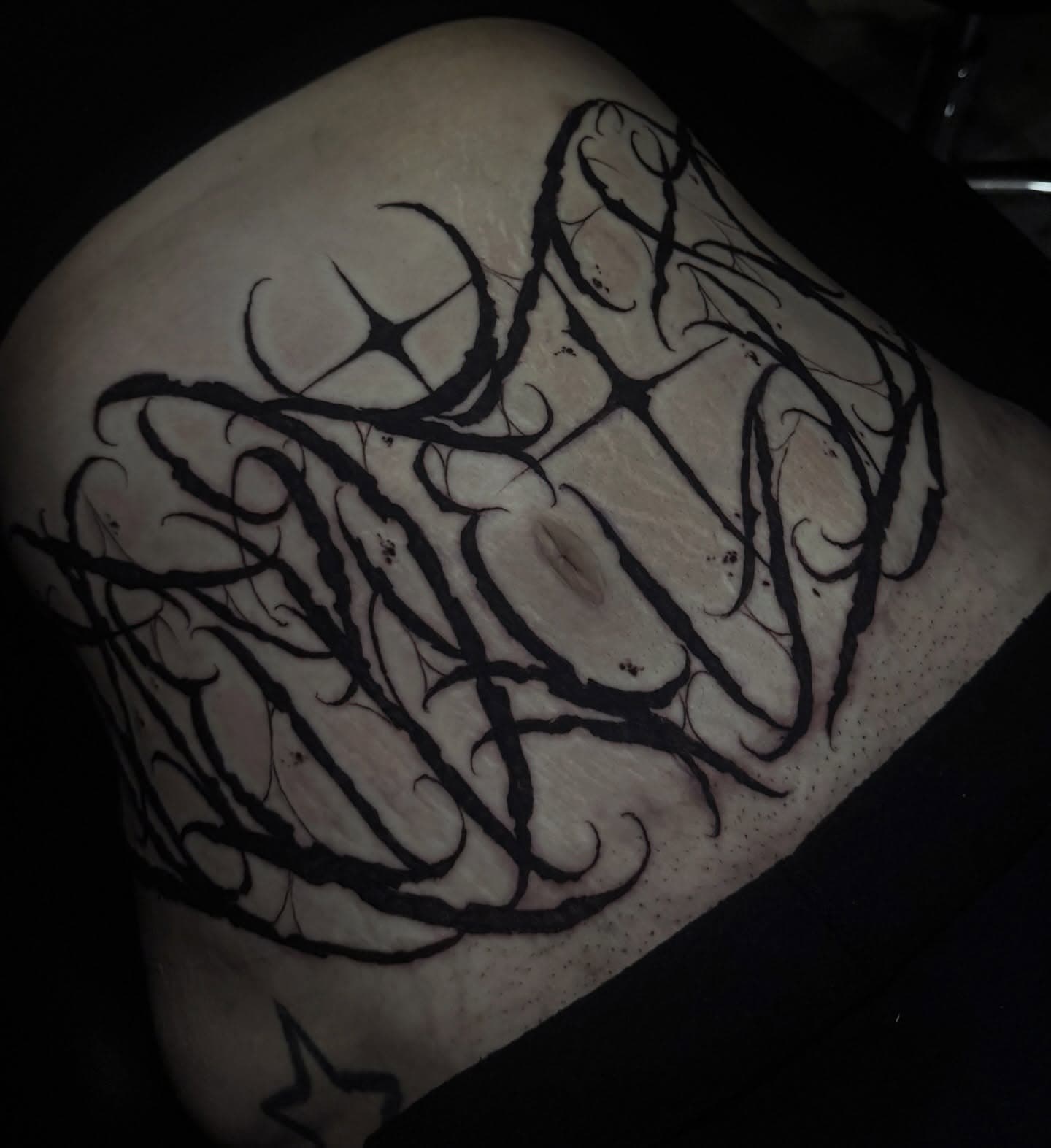 Large gothic script lettering laid across the stomach in bold tapered black strokes that follow the curve of the torso.
