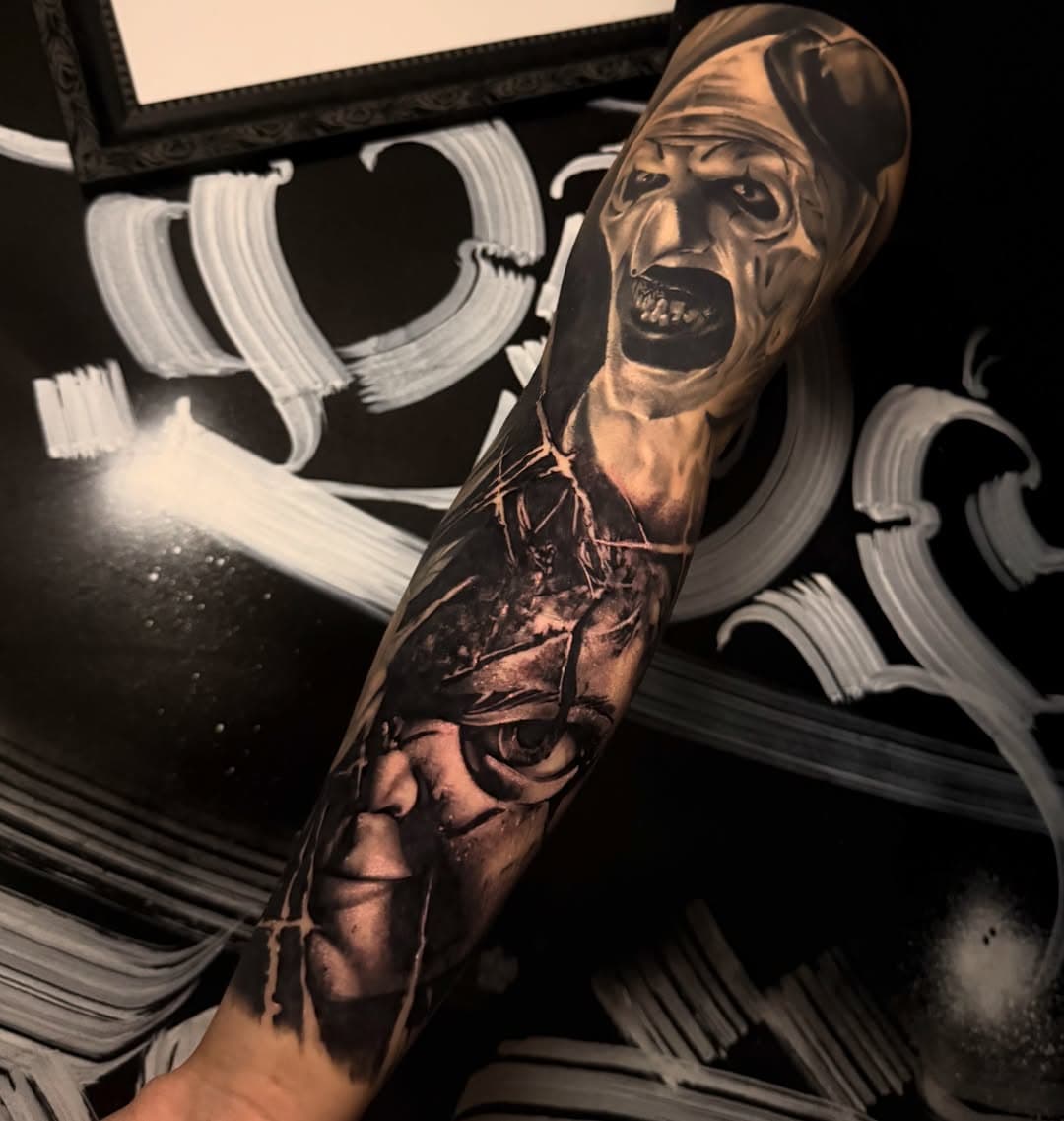Black-and-grey horror forearm sleeve with two stacked clown faces and a cracked-glass background, photographed healed about one year after completion.