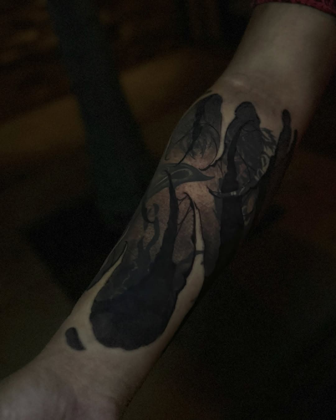 Negative-space blackwork on the forearm where solid black shapes leave bare skin reading as the design, shot in low light.