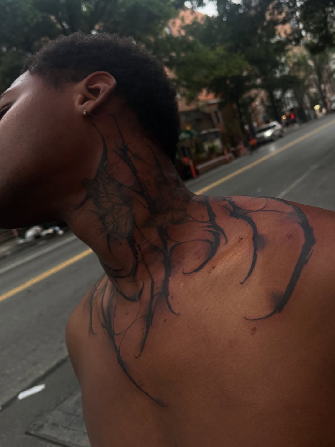 Freehand blackwork running up the side of the neck and out across the shoulder in long tapered strokes, photographed outdoors on a New York street.