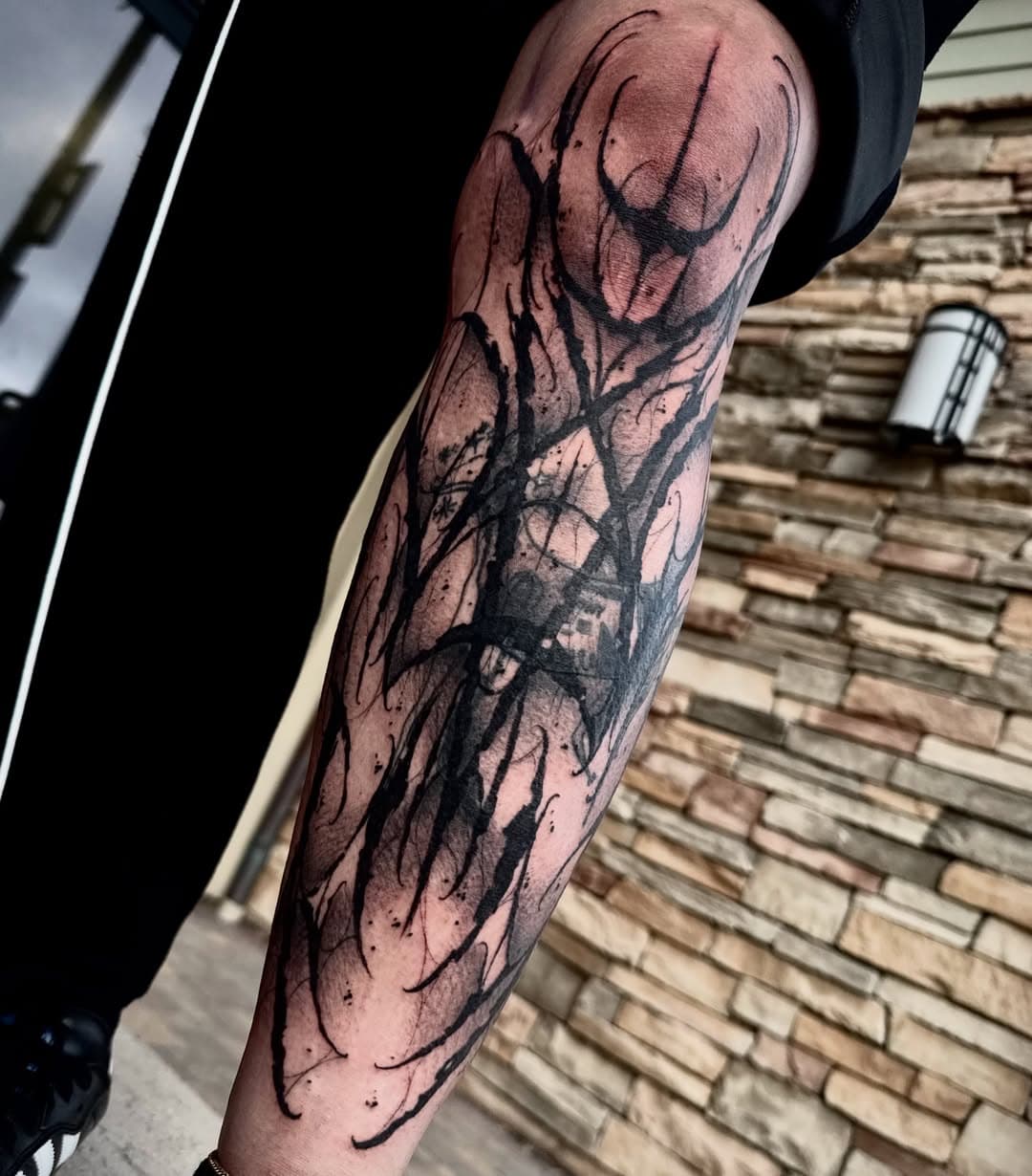 Organic freehand blackwork covering the forearm in sweeping tapered strokes and scattered dots, wrapping with the muscle.